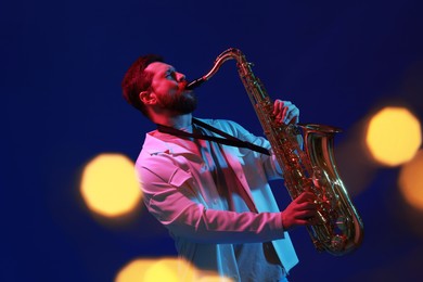 Photo of Professional musician playing saxophone on blue background with blurred lights. Bokeh effect