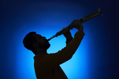 Photo of Professional musician playing soprano saxophone on blue background, backlit