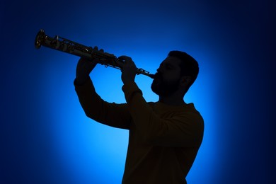 Photo of Professional musician playing soprano saxophone on blue background, backlit