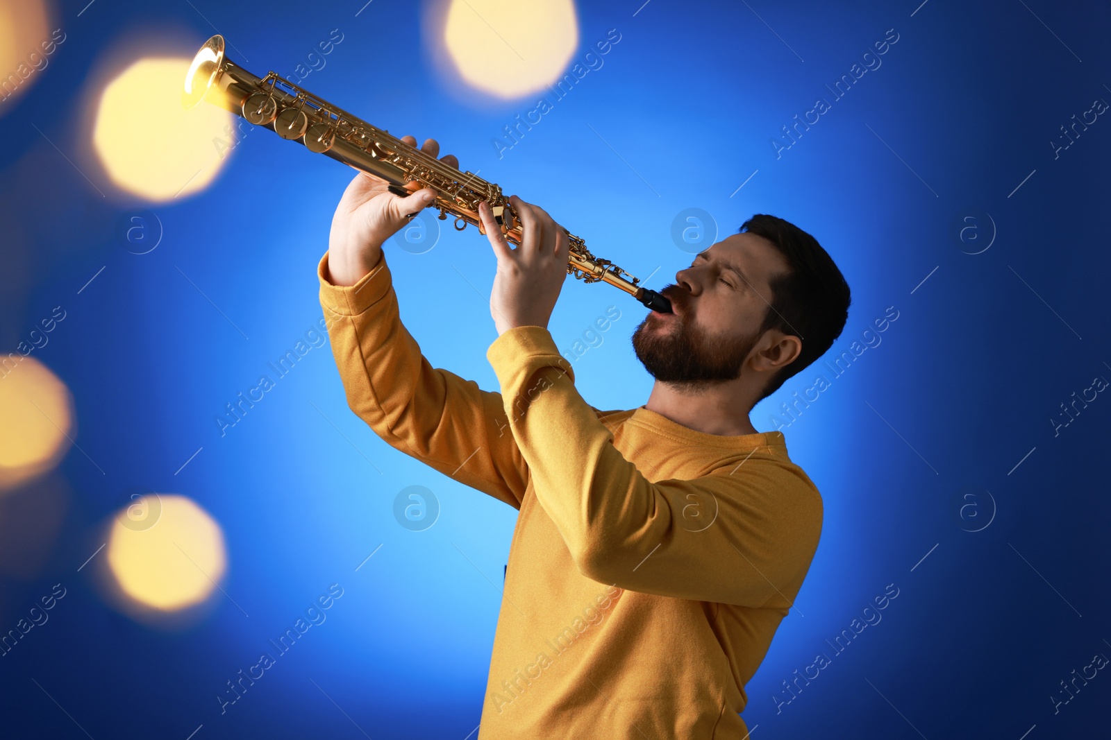 Photo of Professional musician playing soprano saxophone on blue background with blurred lights. Bokeh effect