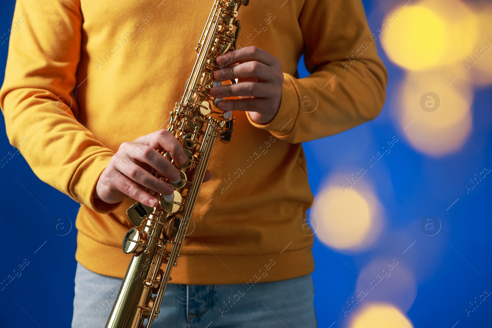 Photo of Professional musician holding soprano saxophone on blue background with blurred lights, closeup. Bokeh effect