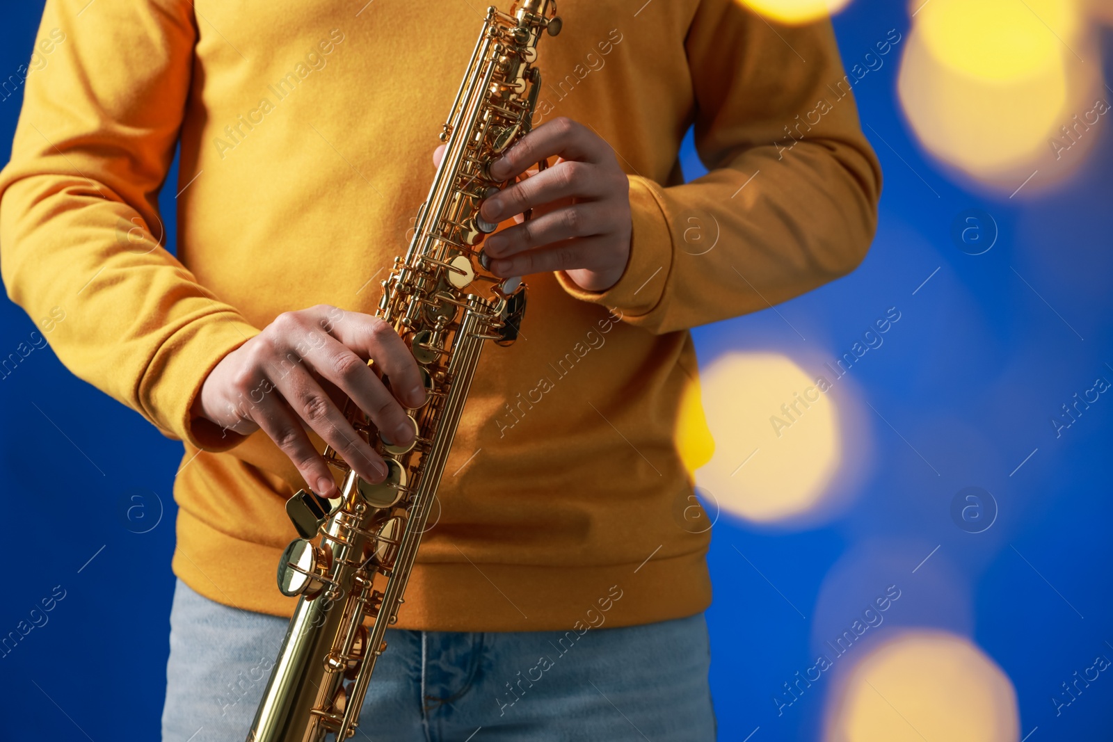 Photo of Professional musician holding soprano saxophone on blue background with blurred lights, closeup. Bokeh effect