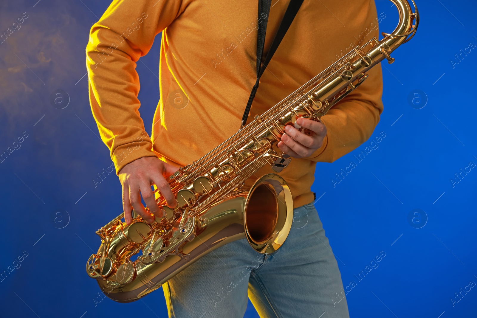 Photo of Professional musician playing saxophone on blue background, closeup