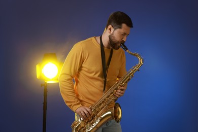 Professional musician playing saxophone on blue background with light