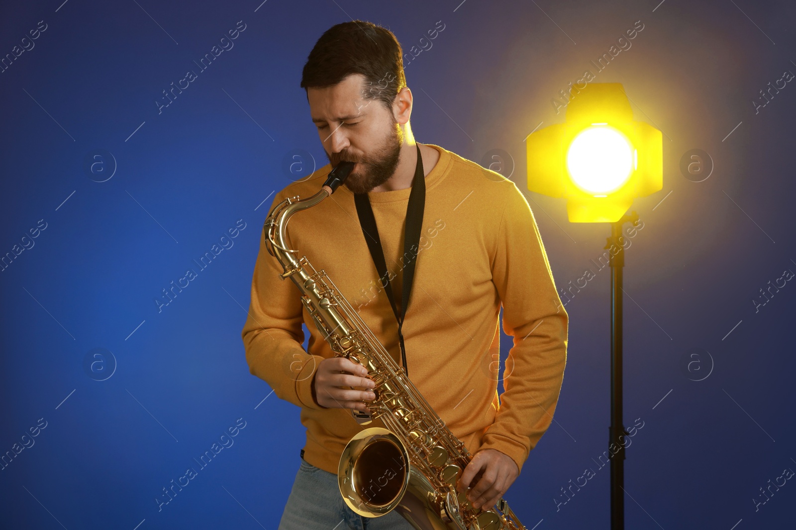 Photo of Professional musician playing saxophone on blue background with light