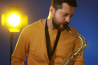 Photo of Professional musician playing saxophone on blue background with light