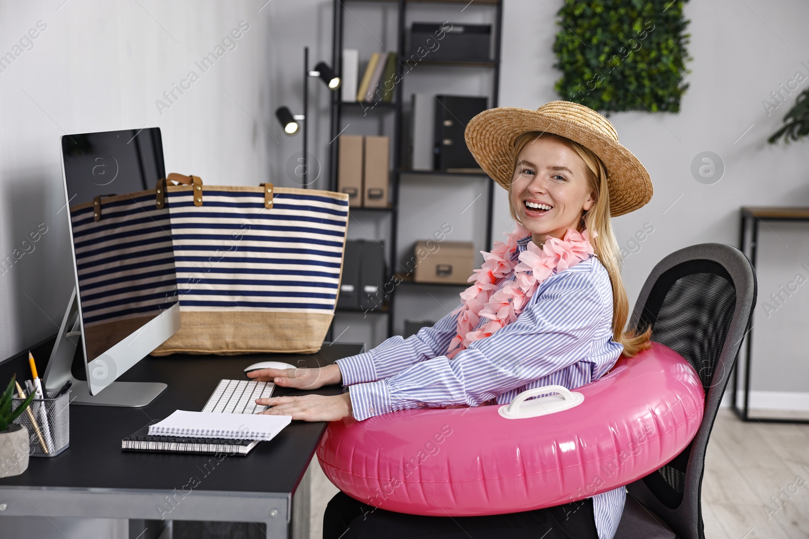 Photo of Businesswoman with inflatable ring, flower wreath, bag and straw hat at workplace in office