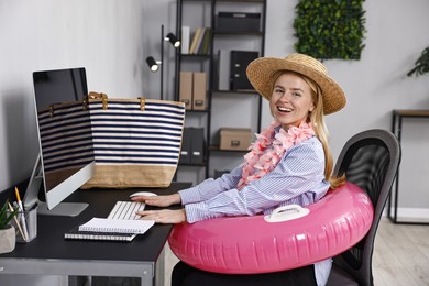 Photo of Businesswoman with inflatable ring, flower wreath, bag and straw hat at workplace in office