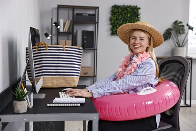 Photo of Businesswoman with inflatable ring, flower wreath, bag and straw hat at workplace in office