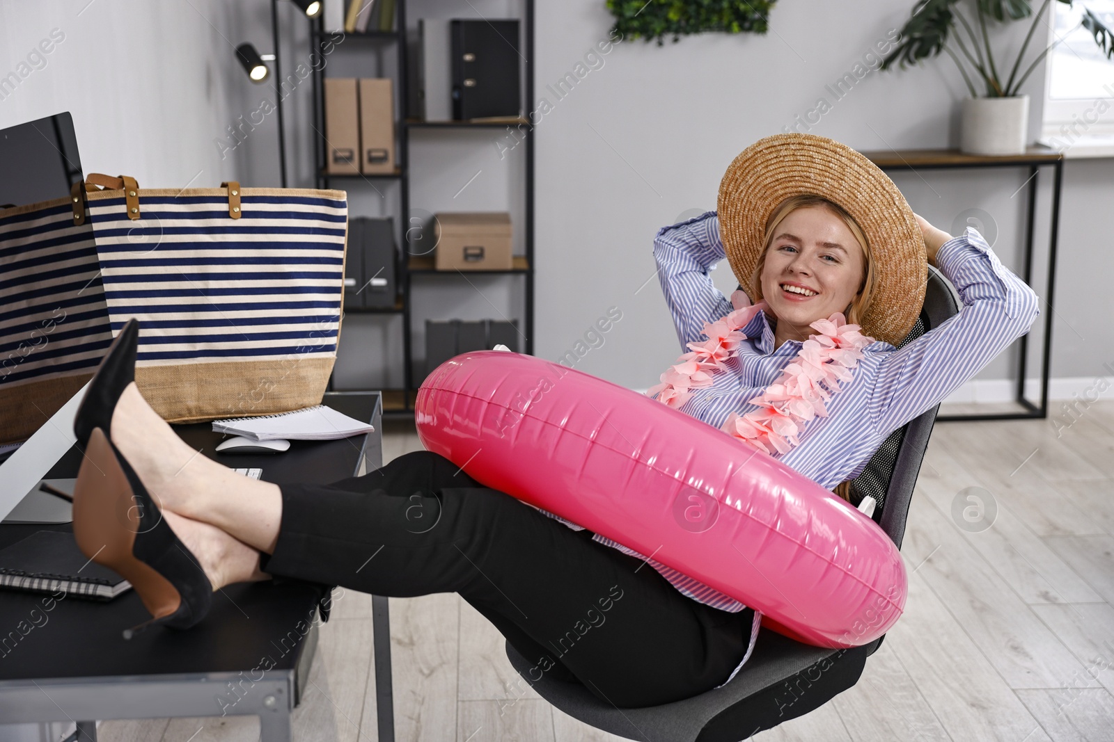 Photo of Businesswoman with inflatable ring, flower wreath, bag and straw hat at workplace in office