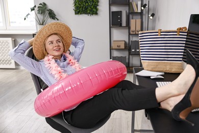 Photo of Businesswoman with inflatable ring, flower wreath, bag and straw hat at workplace in office