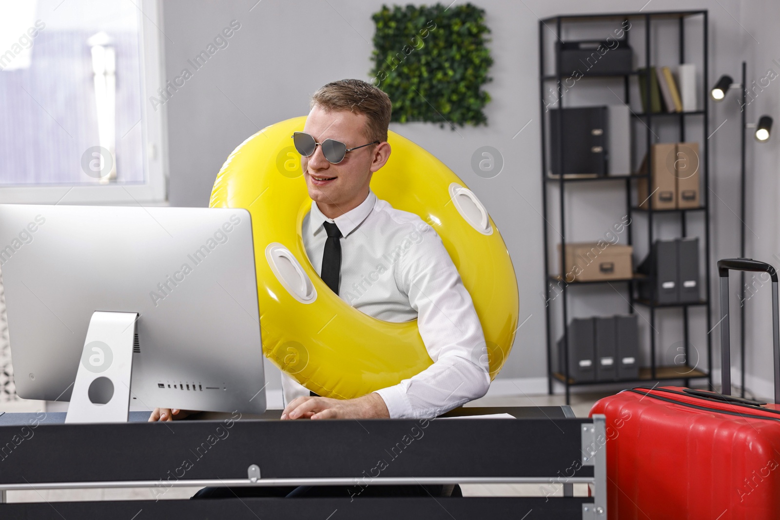 Photo of Businessman with inflatable ring and sunglasses at workplace in office