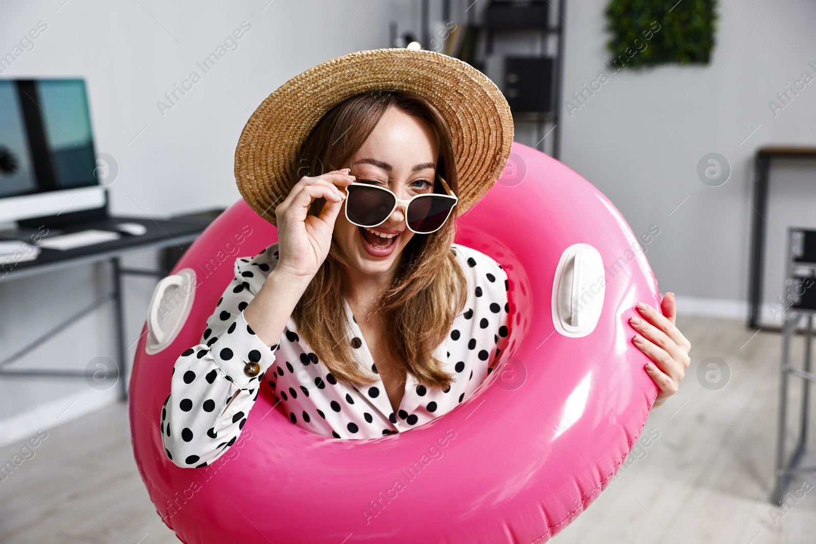 Photo of Businesswoman with inflatable ring, straw hat and sunglasses in office