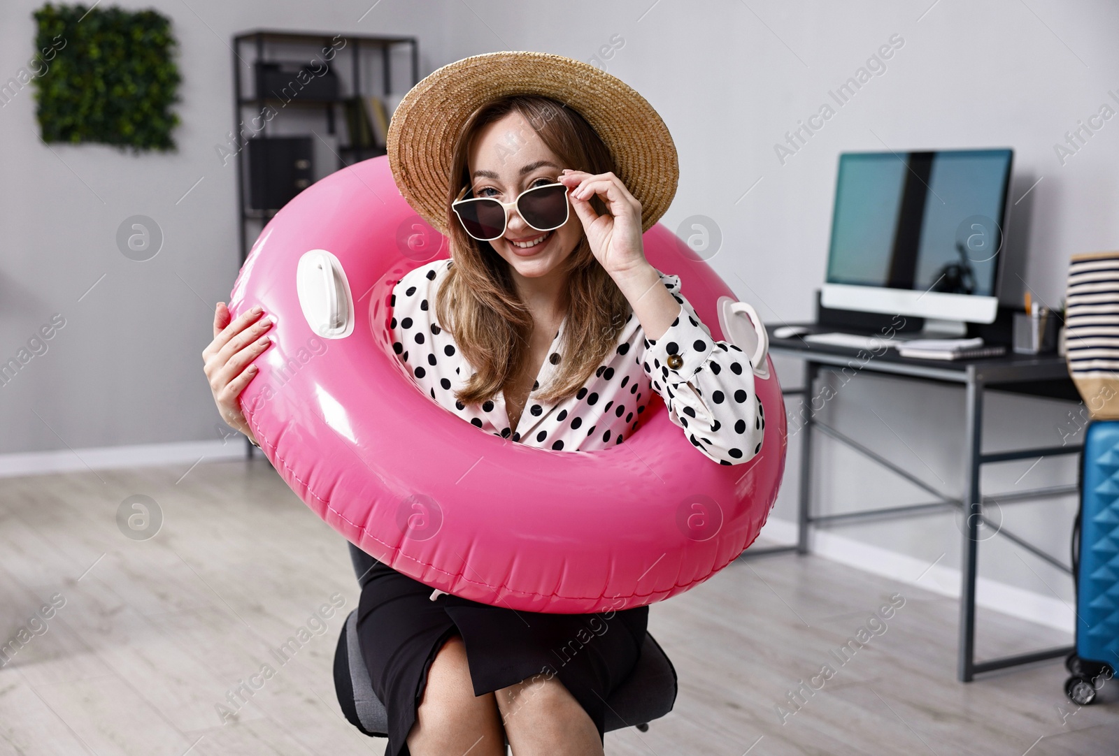 Photo of Businesswoman with inflatable ring, straw hat and sunglasses in office