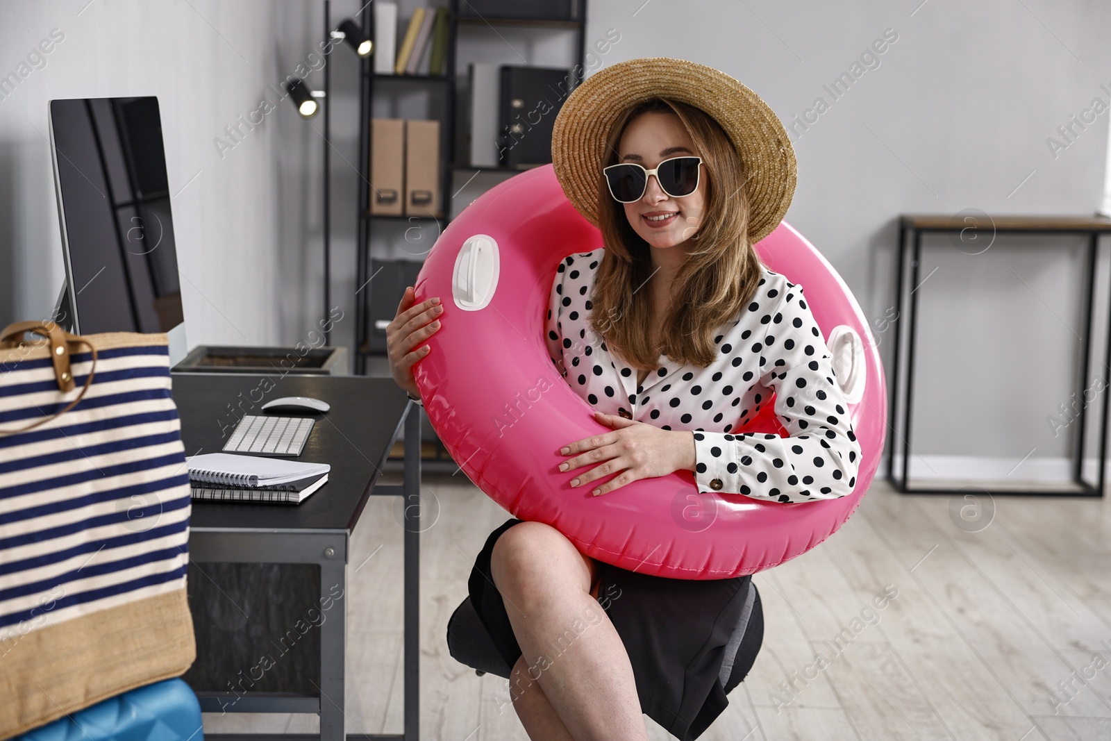 Photo of Businesswoman with inflatable ring, straw hat and sunglasses at workplace in office