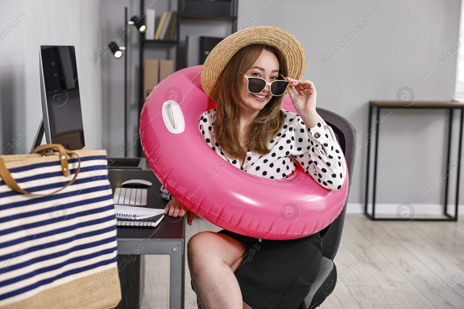 Photo of Businesswoman with inflatable ring, straw hat and sunglasses at workplace in office