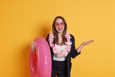 Photo of Businesswoman with inflatable ring, flower wreath and sunglasses on orange background