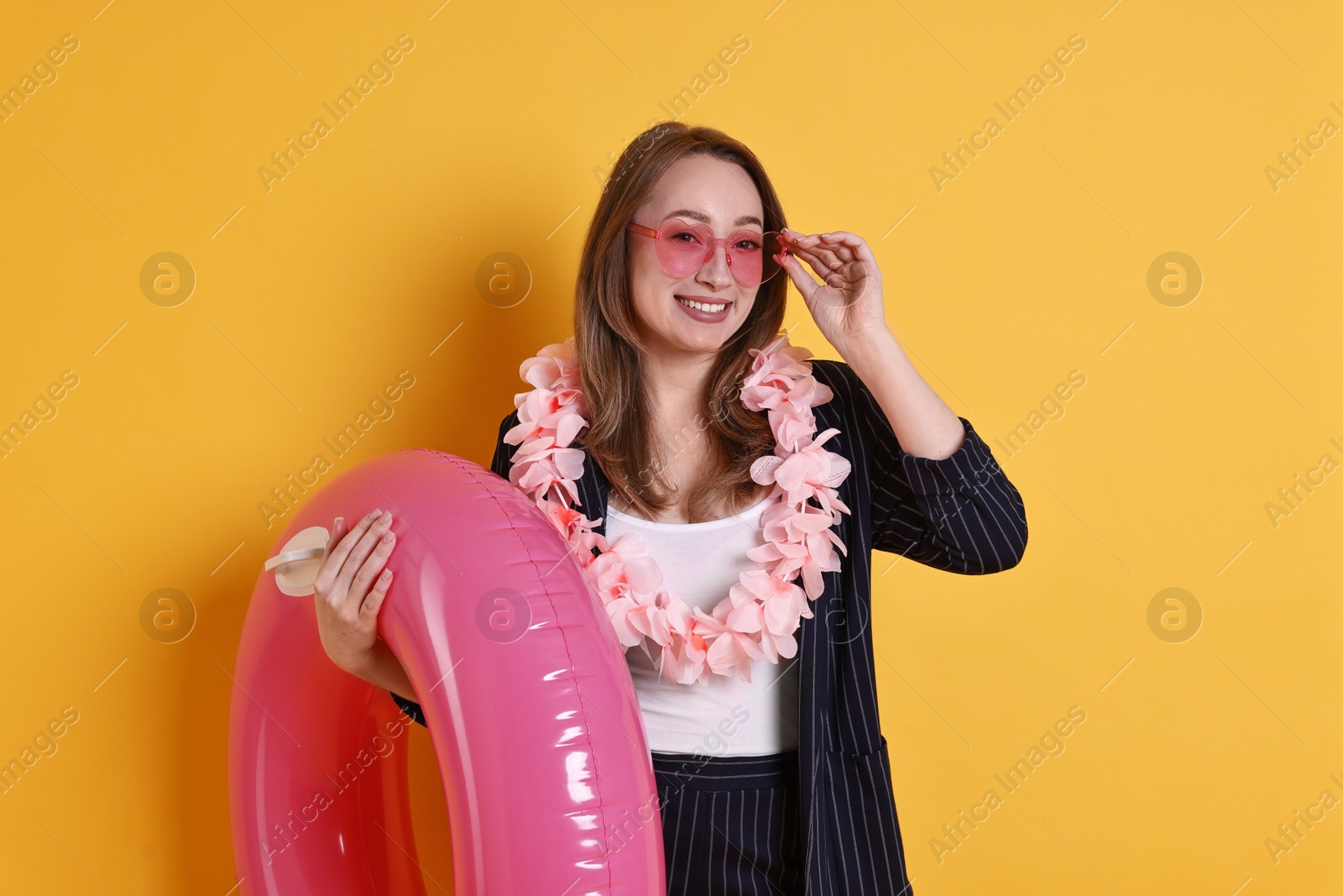 Photo of Businesswoman with inflatable ring, flower wreath and sunglasses on orange background