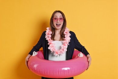 Photo of Surprised businesswoman with inflatable ring, flower wreath and sunglasses on orange background