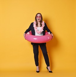 Photo of Surprised businesswoman with inflatable ring, flower wreath and sunglasses on orange background