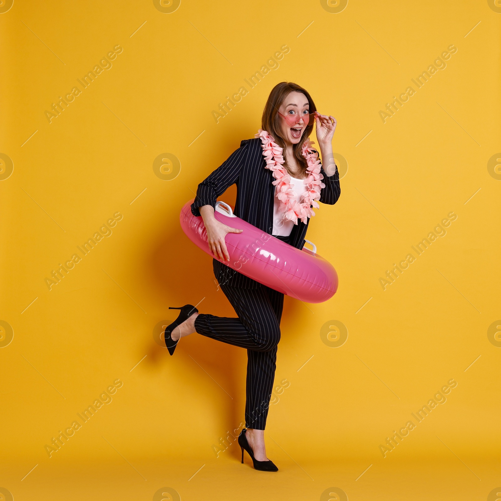 Photo of Emotional businesswoman with inflatable ring, flower wreath and sunglasses posing on orange background