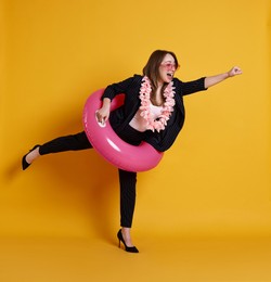 Photo of Emotional businesswoman with inflatable ring, flower wreath and sunglasses posing on orange background