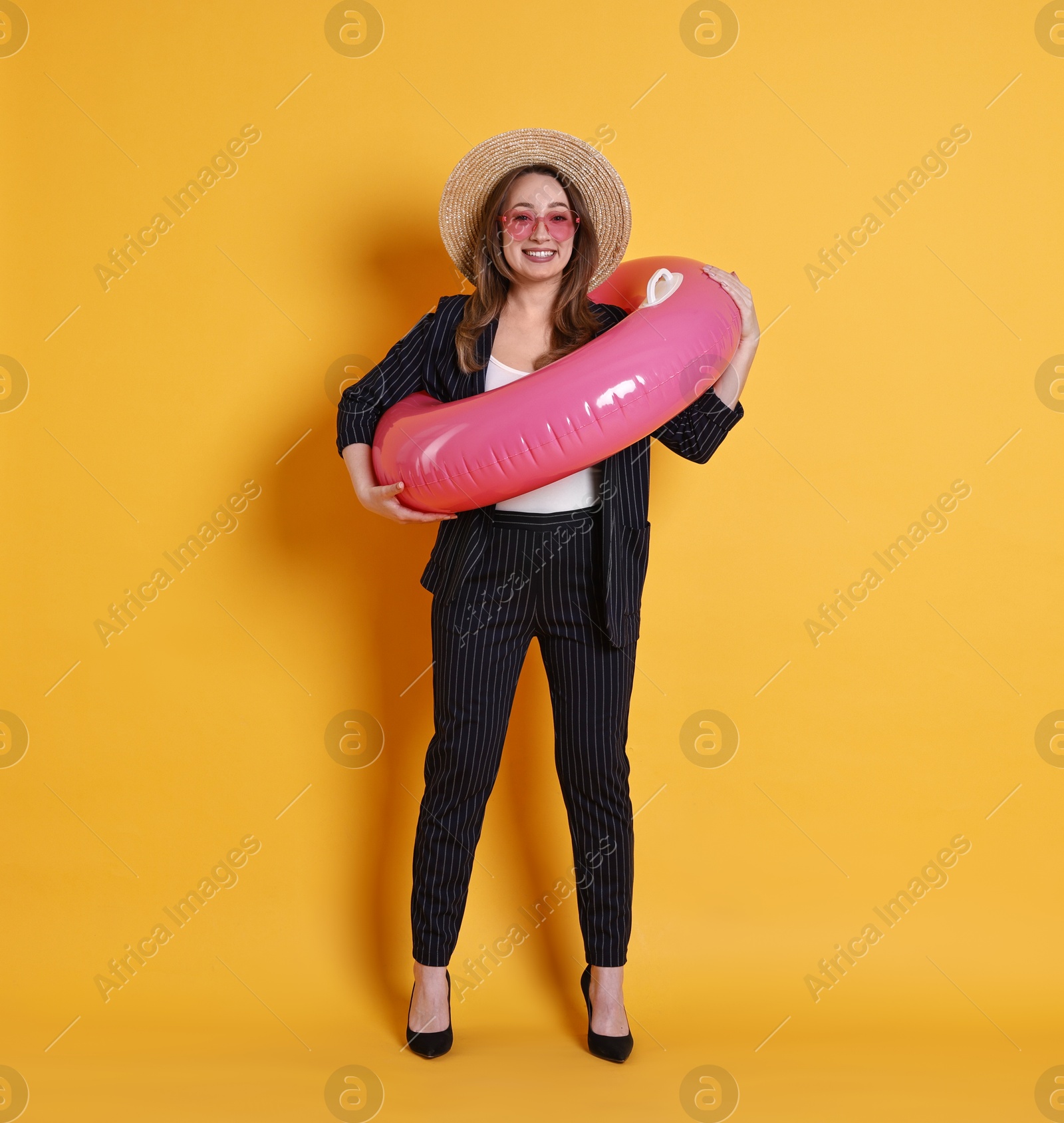 Photo of Businesswoman with inflatable ring, straw hat and sunglasses on orange background