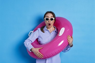 Photo of Surprised businesswoman with inflatable ring and sunglasses on light blue background