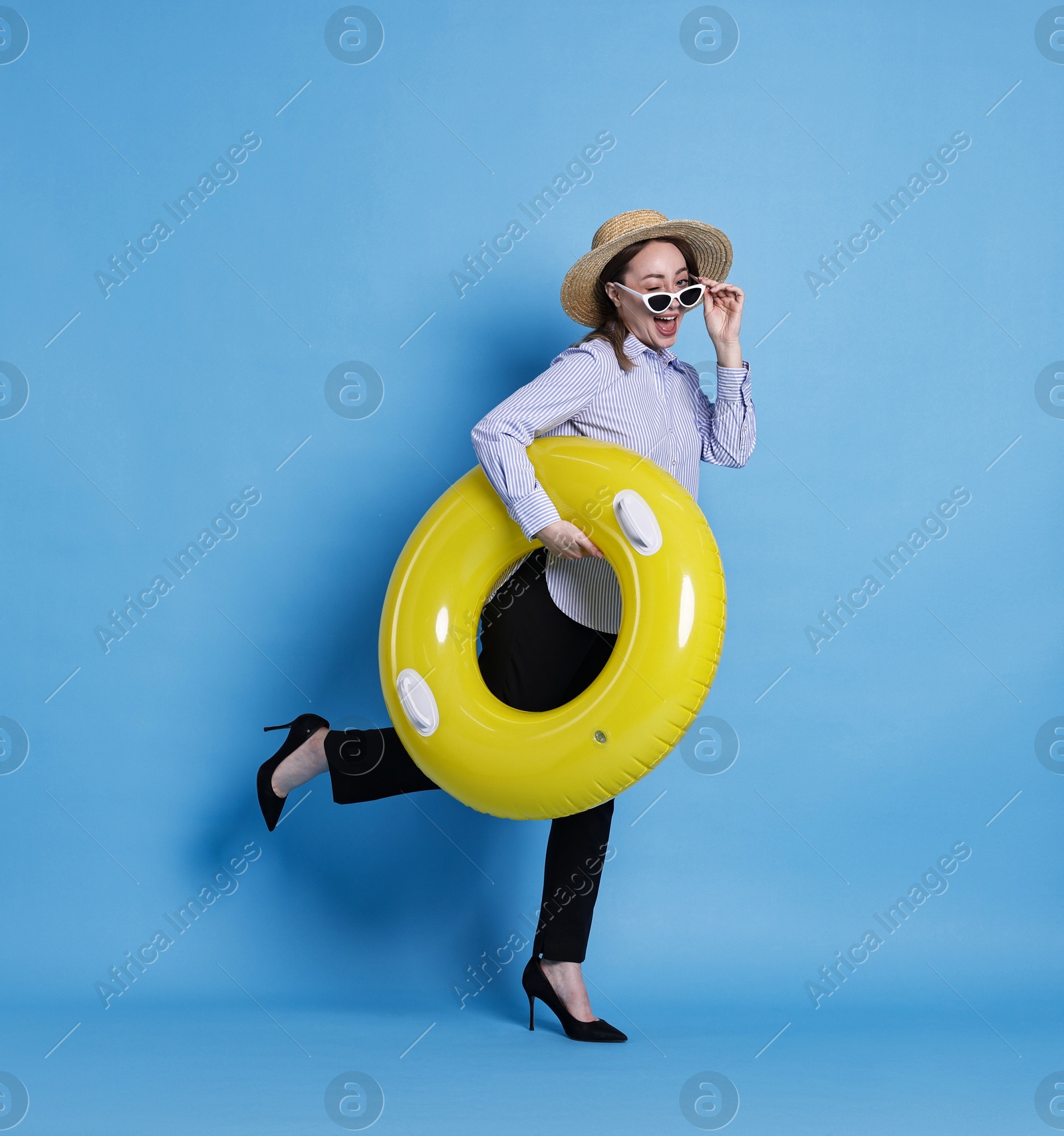 Photo of Businesswoman with inflatable ring, straw hat and sunglasses on light blue background