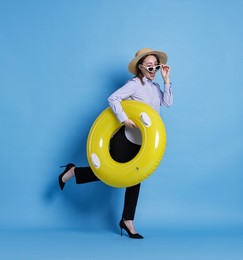 Photo of Businesswoman with inflatable ring, straw hat and sunglasses on light blue background