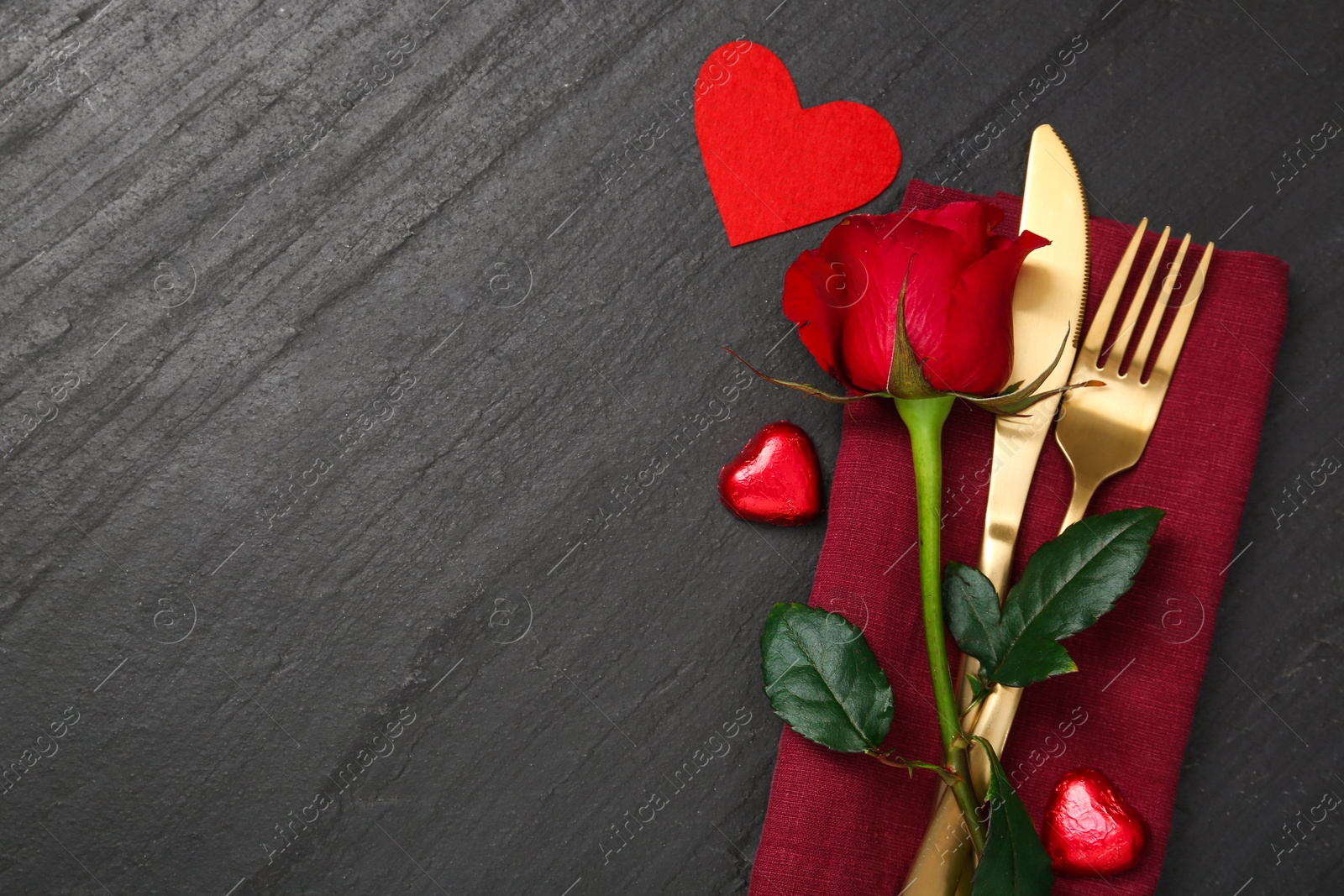 Photo of Romantic place setting with red rose and cutlery on black table, top view. Valentine's day celebration