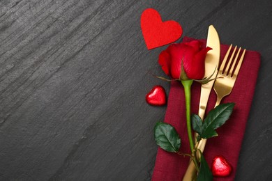 Romantic place setting with red rose and cutlery on black table, top view. Valentine's day celebration