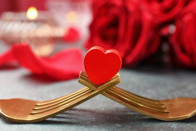 Photo of Golden forks with decorative red heart and roses on grey table, closeup. Valentine's day celebration