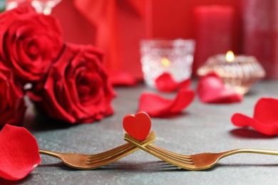 Photo of Golden forks with decorative red heart and roses on grey table, closeup. Valentine's day celebration