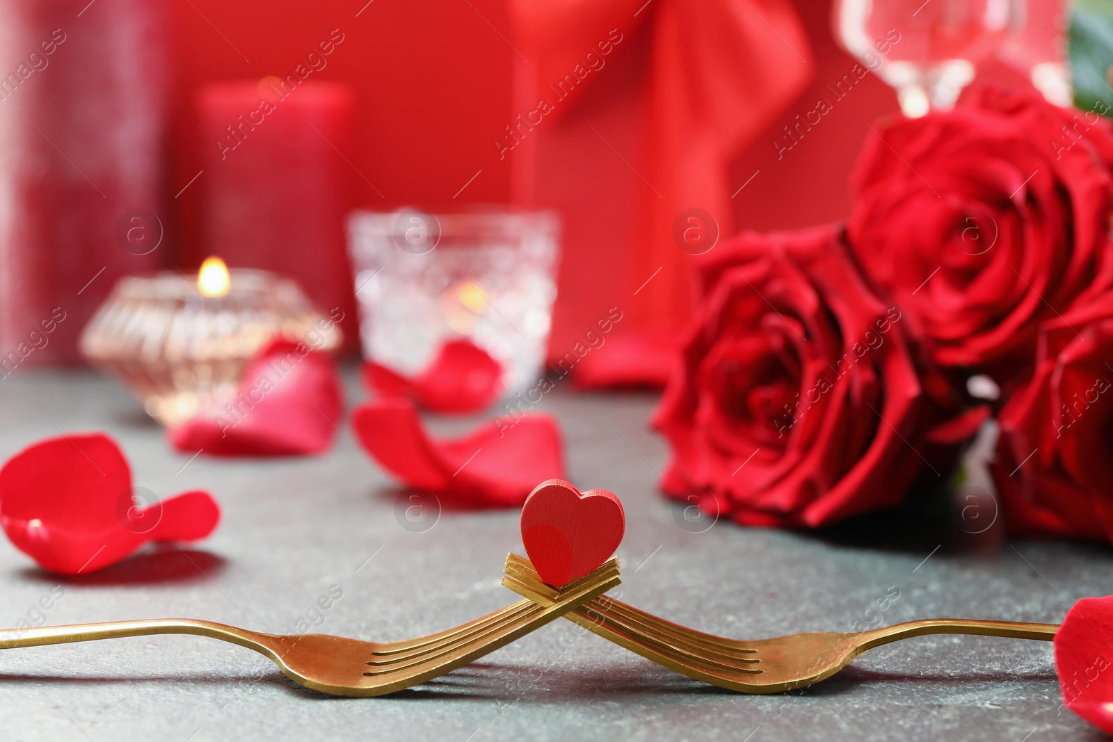 Photo of Golden forks with decorative red heart and roses on grey table, closeup. Valentine's day celebration