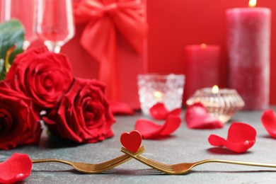 Photo of Golden forks with decorative red heart and roses on grey table, closeup. Valentine's day celebration