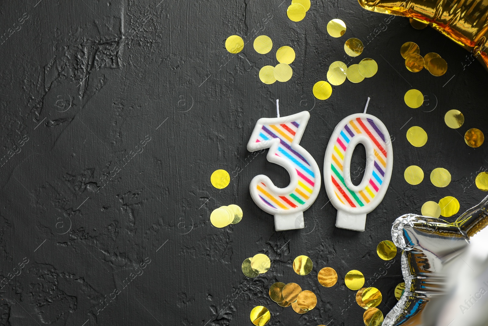 Photo of 30th birthday. Number shaped candles, balloons and confetti on black background, flat lay. Space for text