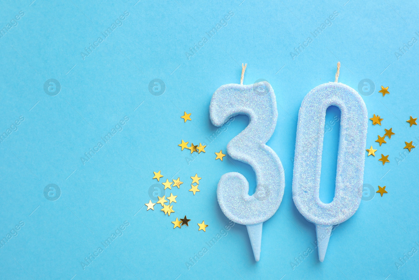 Photo of 30th birthday. Number shaped candles and confetti on light blue background, flat lay. Space for text