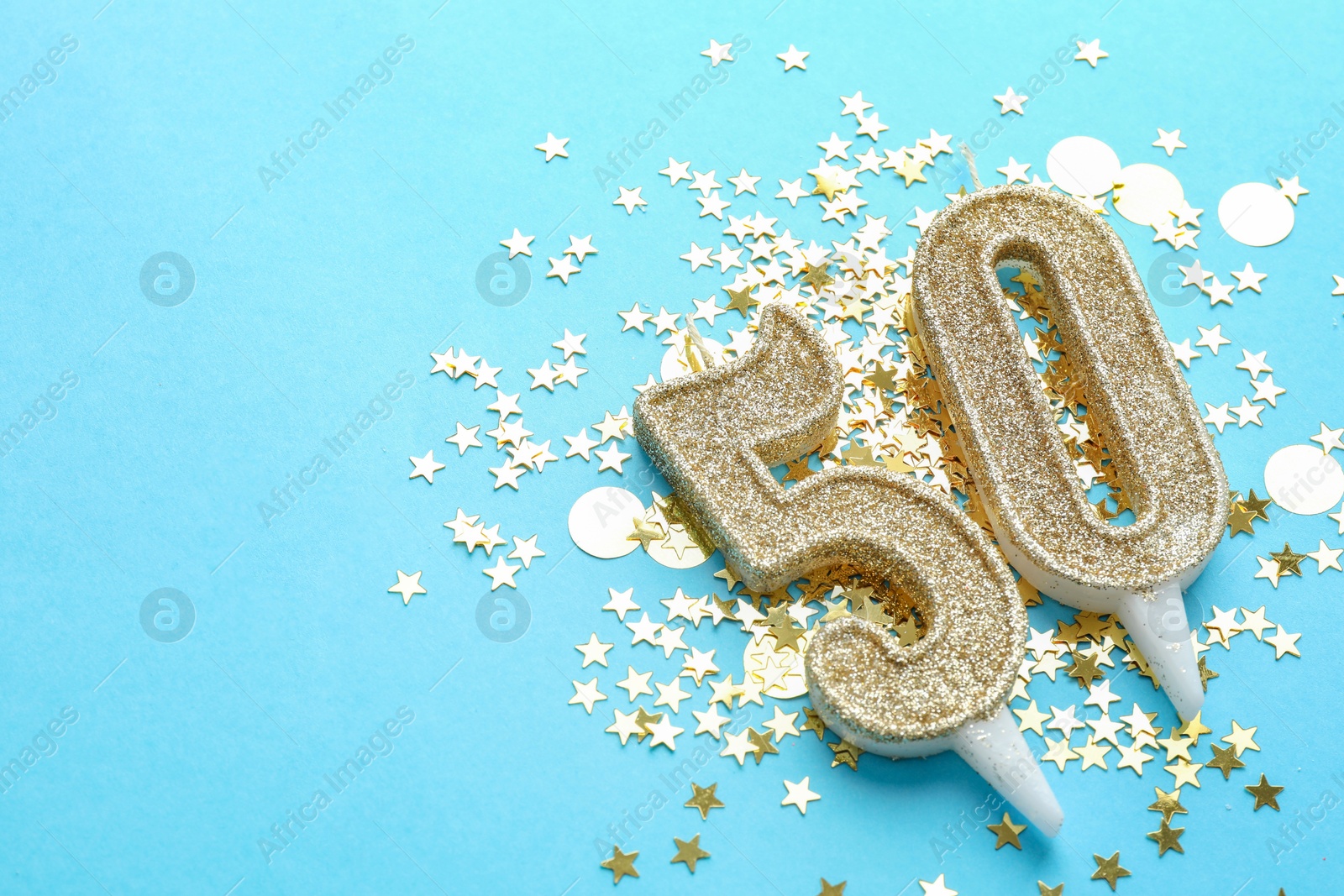 Photo of 50th birthday. Number shaped candles and confetti on light blue background, closeup. Space for text