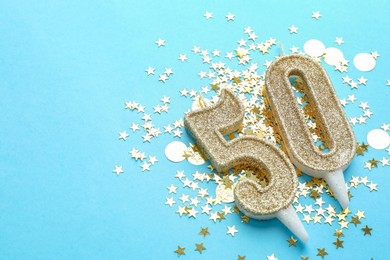 Photo of 50th birthday. Number shaped candles and confetti on light blue background, closeup. Space for text