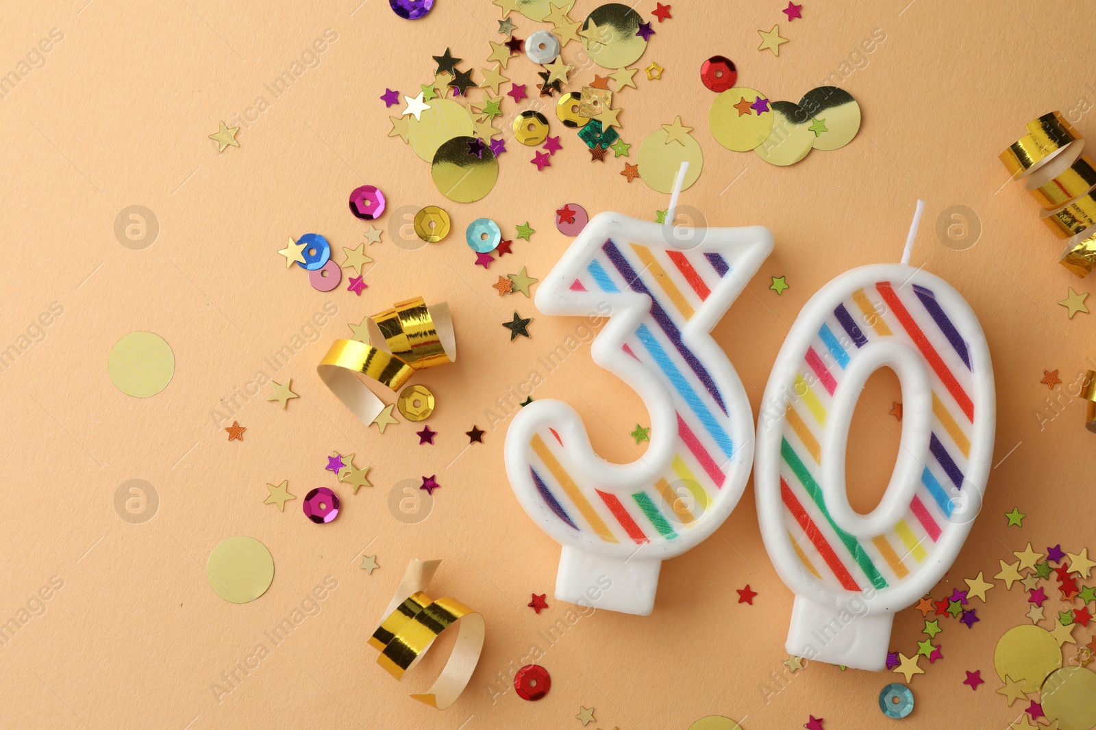 Photo of 30th birthday. Number shaped candles and confetti on beige background, flat lay. Space for text