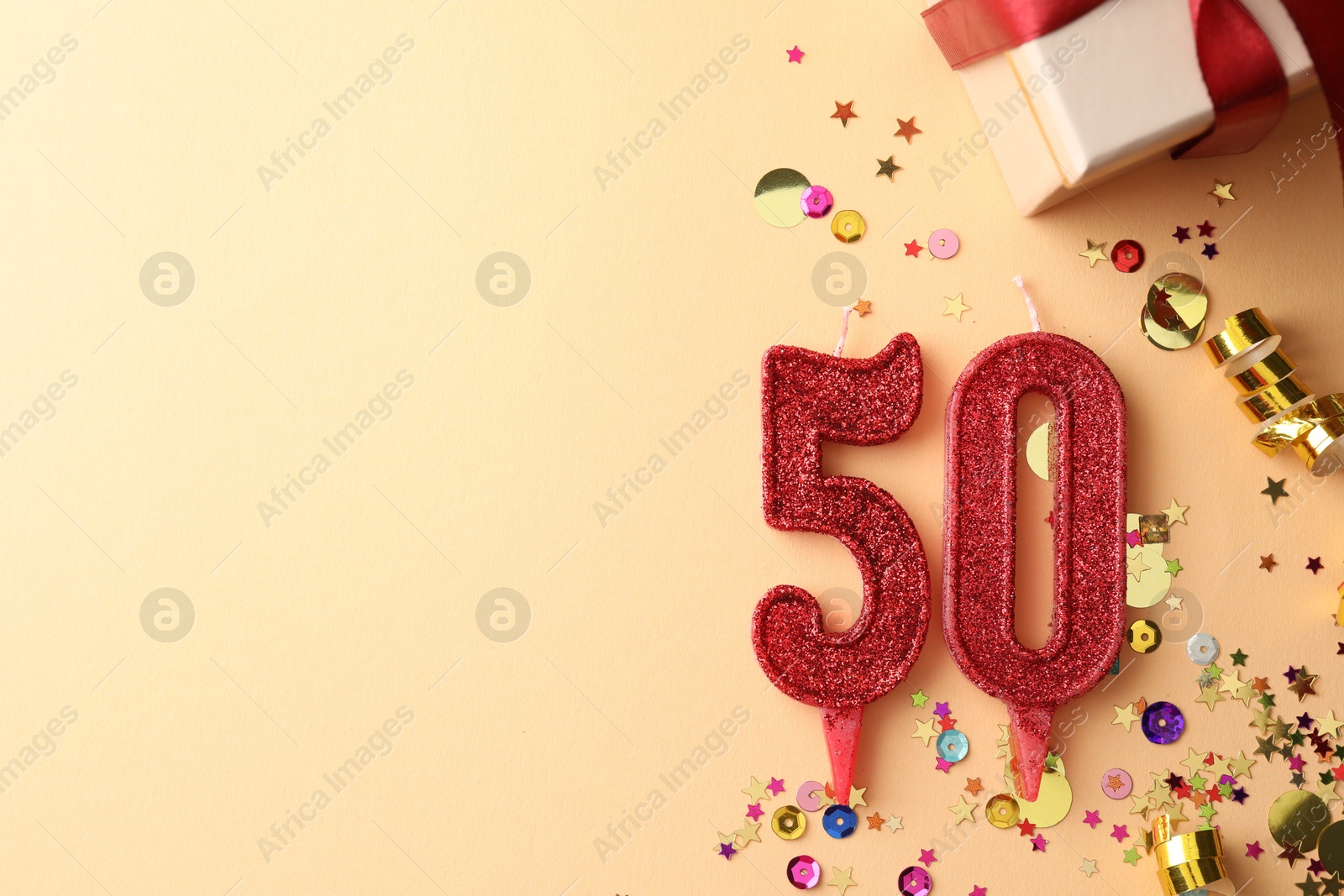 Photo of 50th birthday. Number shaped candles, gift box and confetti on beige background, flat lay. Space for text