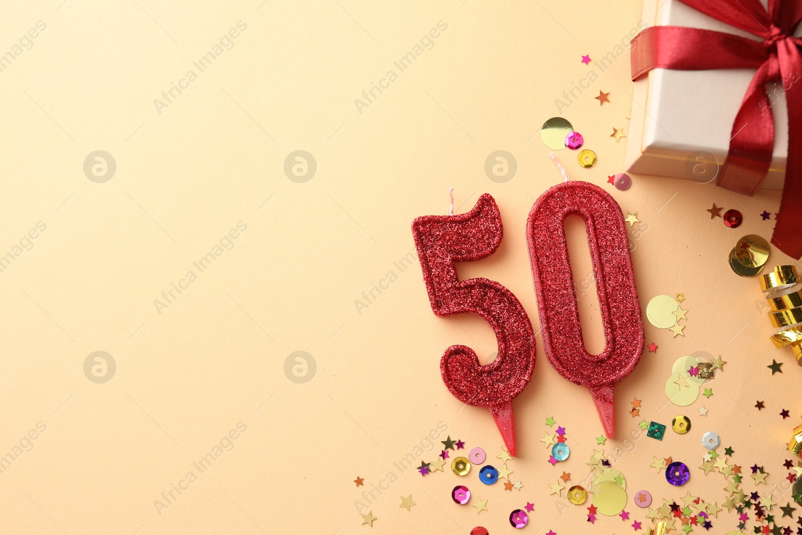 Photo of 50th birthday. Number shaped candles, gift box and confetti on beige background, flat lay. Space for text