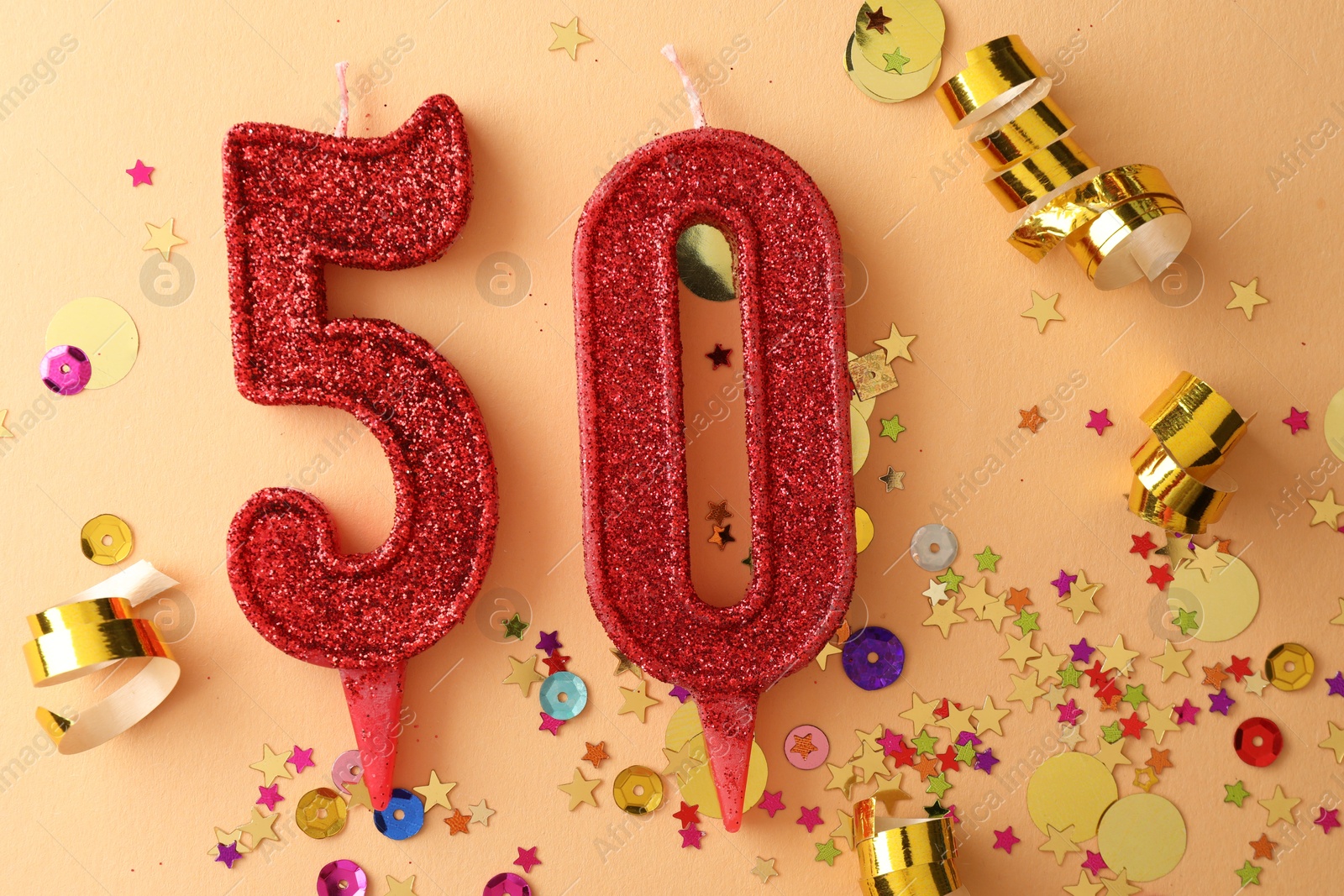 Photo of 50th birthday. Number shaped candles and confetti on beige background, flat lay