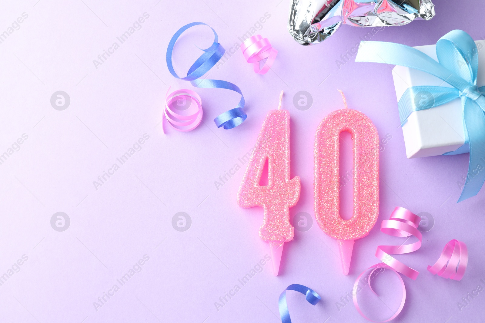 Photo of 40th birthday. Number shaped candles and party decor on violet background, flat lay. Space for text