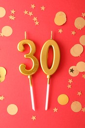 Photo of 30th birthday. Number shaped candles and confetti on red background, flat lay