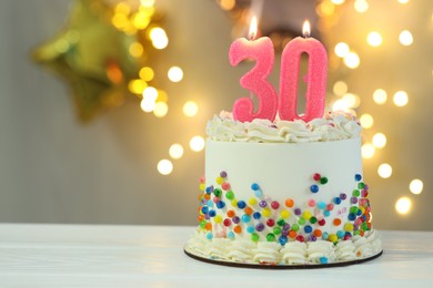 Photo of 30th birthday. Cake with burning number shaped candles on white wooden table against blurred background with lights, closeup and space for text. Bokeh effect