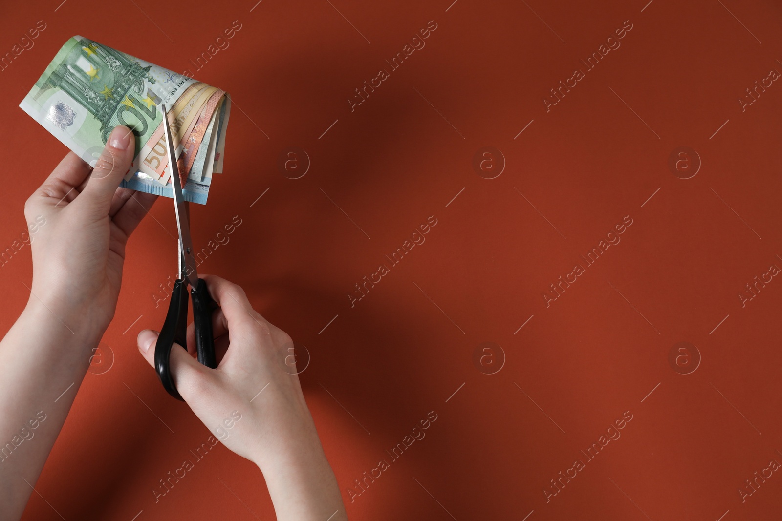 Photo of Woman cutting euro banknotes on brown background, top view. Space for text