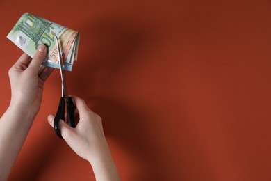 Photo of Woman cutting euro banknotes on brown background, top view. Space for text