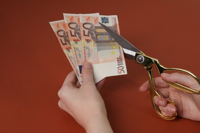 Photo of Woman cutting euro banknotes on brown background, closeup